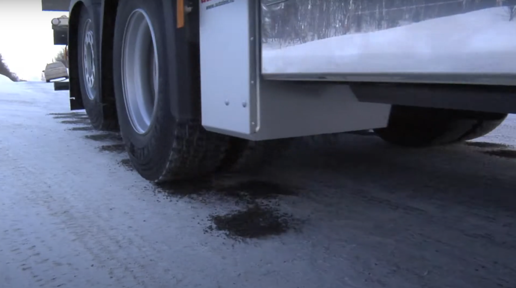 White Autoline sand spreader box dispensing gravel in front of driving wheel. All image credits Autoline